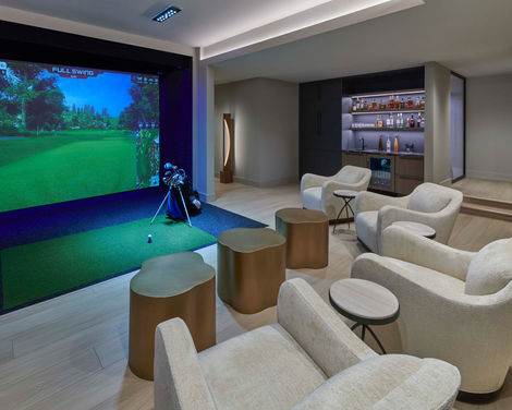 Private golf simulator room with projection screen, lounge seating, and custom built-in beverage bar