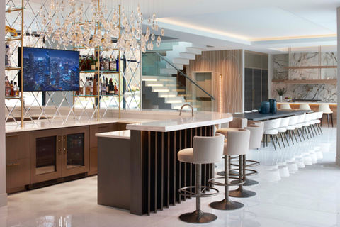 Luxury residential bar with waterfall island, custom wood cabinetry, glass shelving display, and designer bar seating