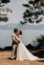 Bride and groom sharing a kiss beside Lake Tahoe shoreline with mountain backdrop.