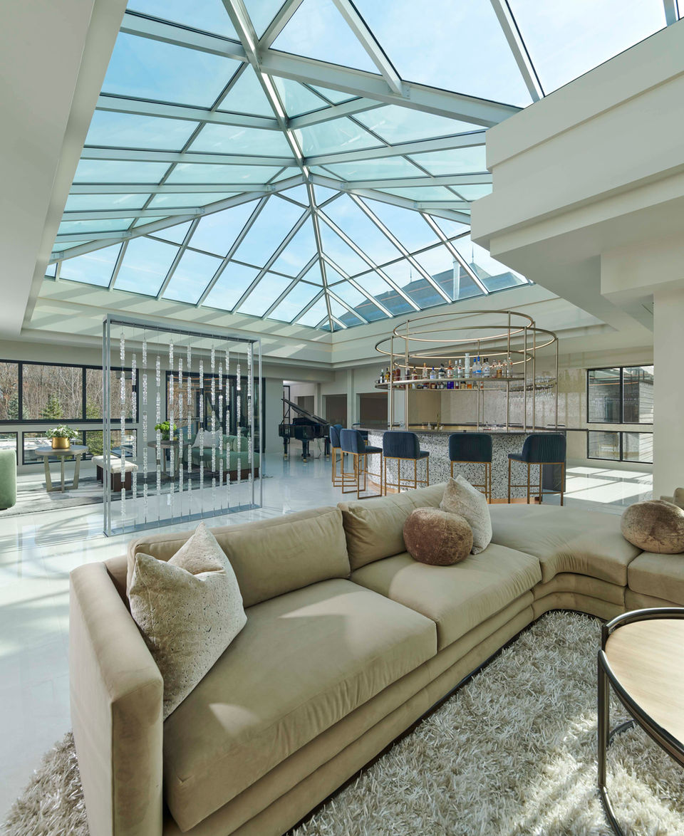 Bright luxury living room with glass ceiling atrium, neutral designer furnishings, and layered interior textures