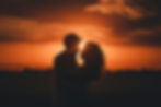 Silhouetted couple embraces against a vibrant orange sunset sky, conveying romance. The serene landscape enhances the intimate mood.