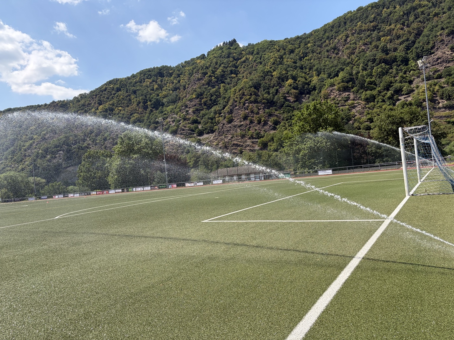Professionelle Beregnungsanlage bewässert einen Fußballplatz im Sonnenschein