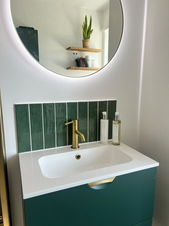 Compact bathroom vanity with green unit, round LED mirror, brass tap and heated towel rail with towe