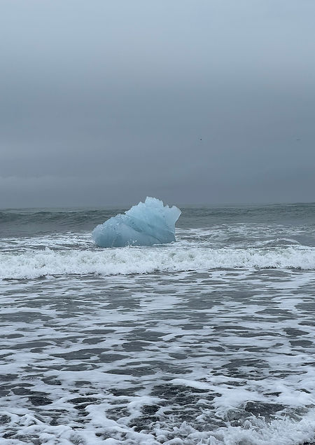 Blue iceberg floating in the clear ocean near the black sand shore of Diamond Beach, Iceland.
