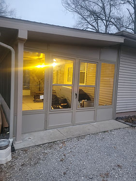 Aluminum-framed glass room with French doors, lit from inside at dusk.