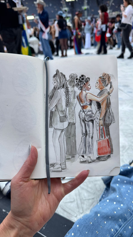 [lang=en] Monochrome and pencil studies of people queuing and resting on the stadium floor, with hats, boots and fringed chaps; the arena blurs behind. Live sketchbook studies of fans at a stadium show, capturing outfits and energy.