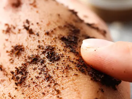 Fingers applying a dark scrub to skin, showing texture. Close-up, light background. Skin exfoliation process.