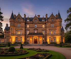 Elegant Scottish estate building at dusk featuring traditional Highland architecture with stone facade, grand entrance with classical columns, manicured formal gardens with pristine lawns and ornamental landscaping, warm ambient lighting creating a luxurious and welcoming hospitality atmosphere