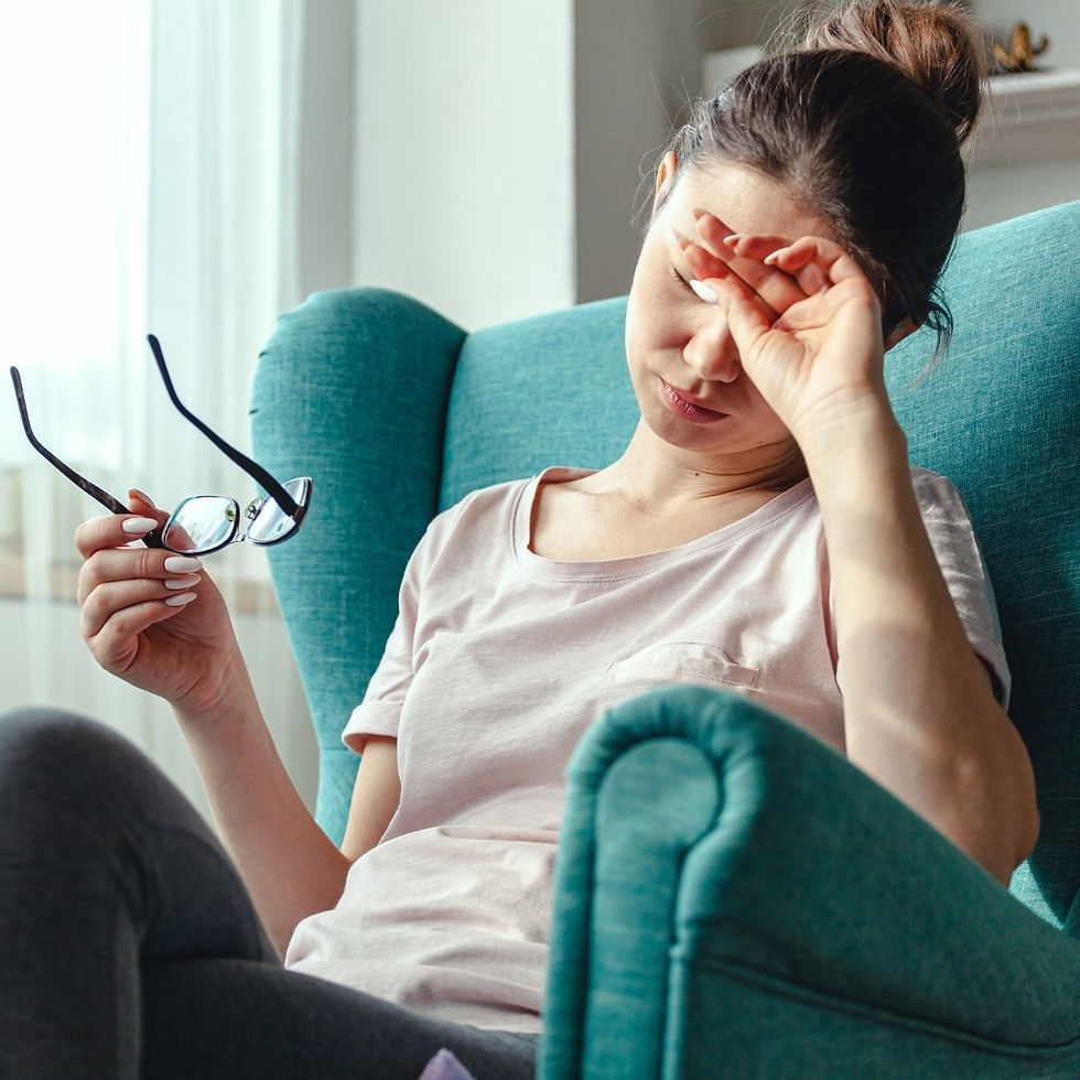 nłoda kobieta siedzi na zielonym fotelu. Ma przechyloną głowę, zamknięte oczy i boli ją głowa. W ręce trzyma okulary