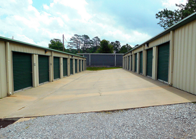 A wide driveway between two self storage buildings with green doors at a facility that offers affordable storage units near Pineville, LA.