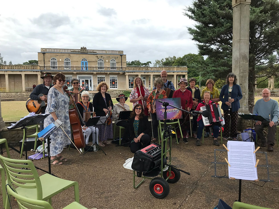 A group of people of all ages pose with their instruments in front of the Waterloo Pavilion, a grand building with tall pillars that houses The Feed Cafe in the background.