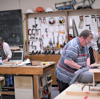 A photo of the workshop in TMP HQ in Oak Street. The walls are covered in tools and in the foreground, a man with short brown hair works at a workbench.