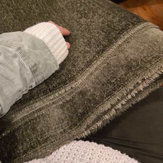 Close-up of hand holding textured fabric for reupholstering mid-century dining chairs.