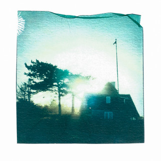 Polaroid emulsion lift showing a thatched house on a beach in sunset