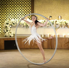 A performer elegantly spinning inside a large metallic Cyr wheel, seamlessly blending acrobatics and artistry against the romantic backdrop of a beautifully decorated wedding venue and a very mesmerised bridal party!
