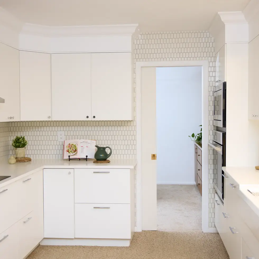 Bright white kitchen with minimalist cabinetry, subway tile backsplash, and natural light streaming through windows.