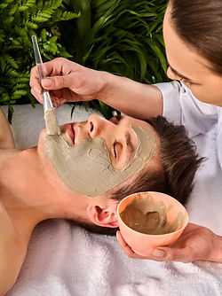 Mud facial mask of man in spa salon. Massage with clay full face. Girl on with therapy roo