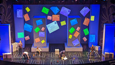 Overlapping text projections fill the stage while cast members hold letters on sticks, amplifying Christopher’s discovery of years of hidden letters from his mother.