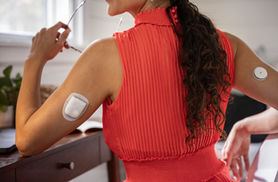 Female wearing Omnipod patch insulin pump on upper arm with CGM sensor on other arm.