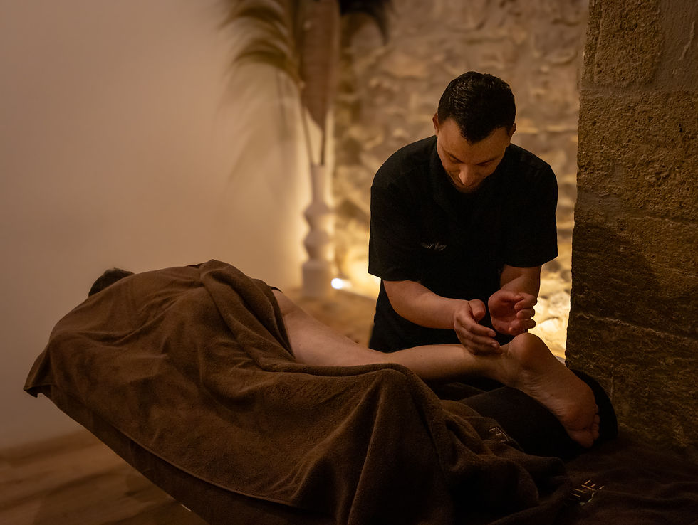 Thérapeute en spa massant le pied d’un client allongé sous une serviette brune, ambiance chaleureuse et tamisée.