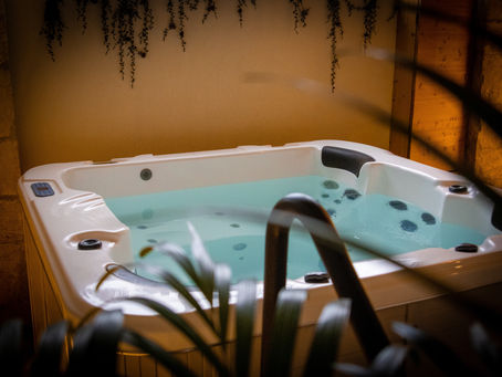 Spa blanc rempli d’eau bleutée dans un décor chaleureux, vu derrière des plantes, ambiance calme.