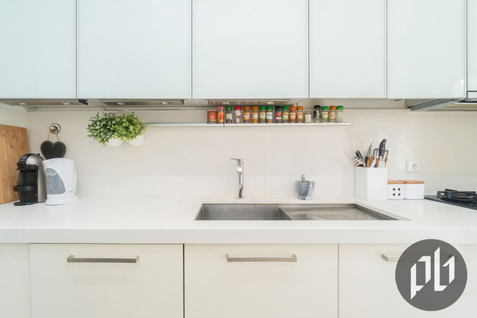 Bancada de cozinha branca minimalista com coleção de frascos de temperos, cafeteira e chaleira.