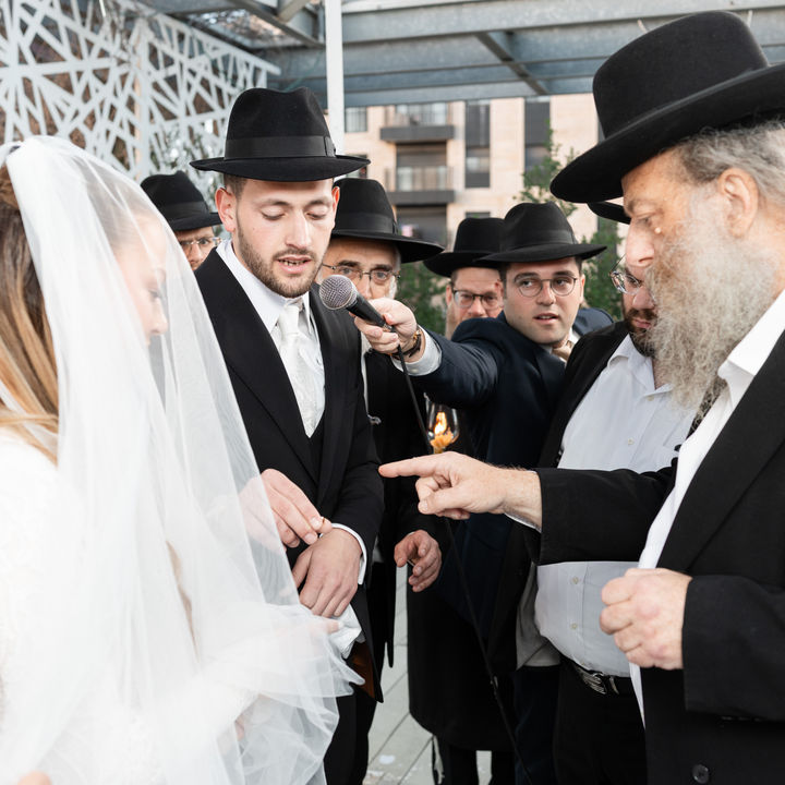 A bride and groom with guests beneath a bright chuppah.