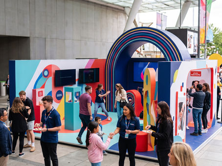 Activación de marca interactiva en un espacio público con estand colorido, personal de marca y asistentes participando.