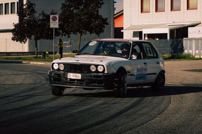 BMW E30 bianca in uscita di curva davanti ai capannoni