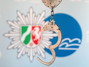 Handschellen geöffnet vor dem Logo des Landes Nordrhein-Westfalen NRW und des Kreises Rhein-Berg