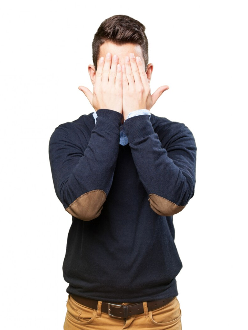 a man with his hands covering his face, he is wearing a blue sweater with brown, suede elbow patches and mustard colored jeans with a brown belt