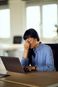 Woman rubbing tired eyes while looking at a computer screen illustrating digital eye strain and dry eye from prolonged screen time.