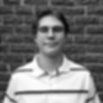 Young man with glasses poses in front of a brick wall background.