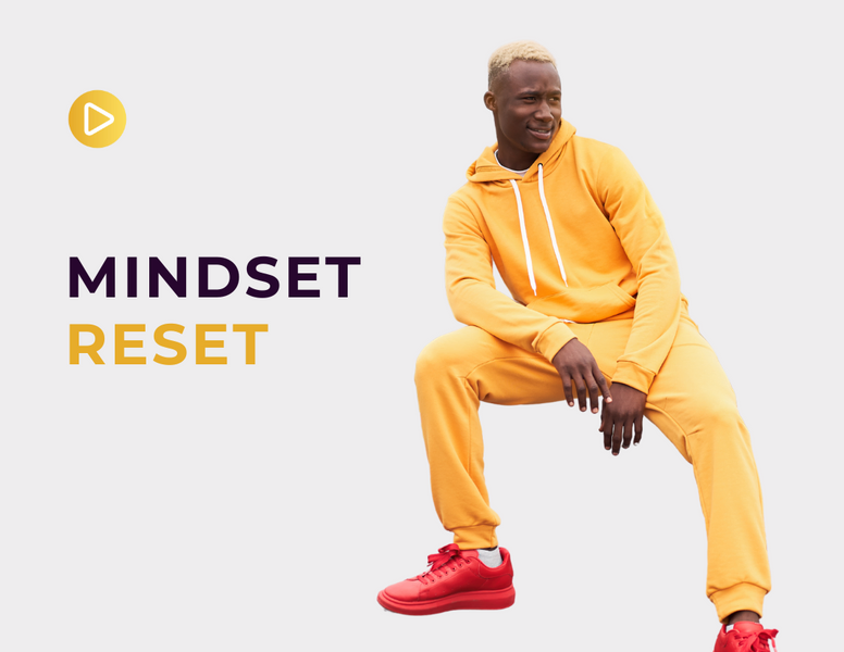 a man in a yellow hoodie sits in front of a sign that says mindset reset
