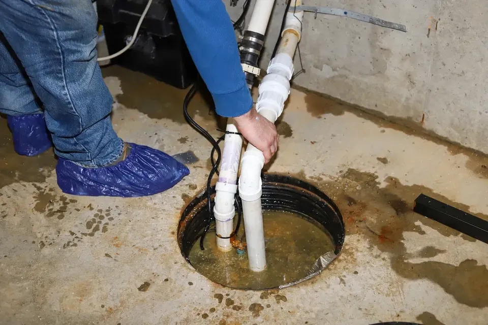 The Home Tradesman inspecting and cleaning a sump pump pit in a Michigan basement.