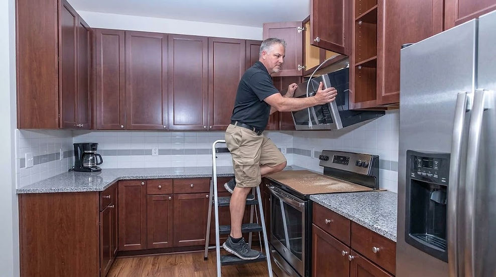 The Home Tradesman contractor installing a microwave oven above a range in a modern kitchen.