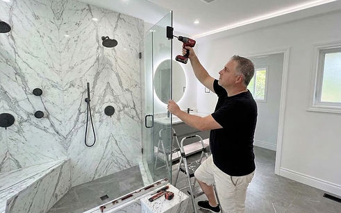 The Home Tradesman contractor installing a glass shower door in a modern bathroom.