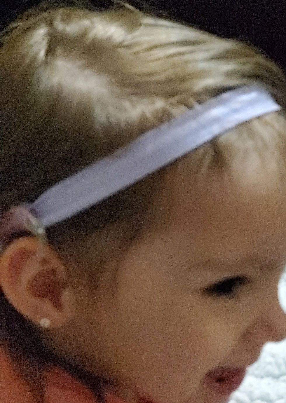 Young child with lavender headband and earring; close-up view.