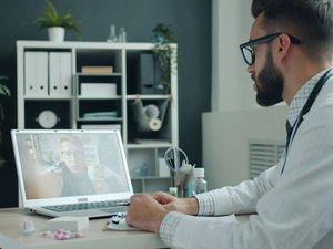 Doctor conducting a telehealth video consultation with a patient on a laptop in a modern healthcare office.