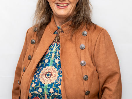 Confident woman in glasses wearing a brown jacket, professional business portrait on a neutral background.