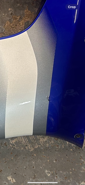 Thumbnail: Close-up of a motorcycle side panel with silver, white, and blue paint.