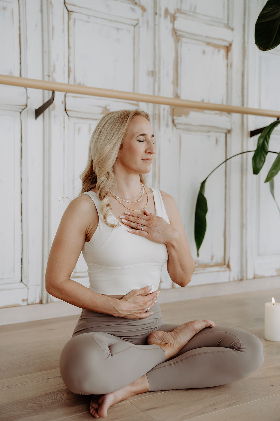 Christine Lindner sitzt in entspannter Meditation mit einer Hand auf dem Herzen in einem lichtdurchfluteten Raum und geschlossenen Augen – herzliche und achtsame Yogalehrerin Chridaya Graz