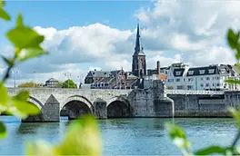 Maastricht: the stone arches of the Sint Servaasbrug over the Maas, framed by leaves.