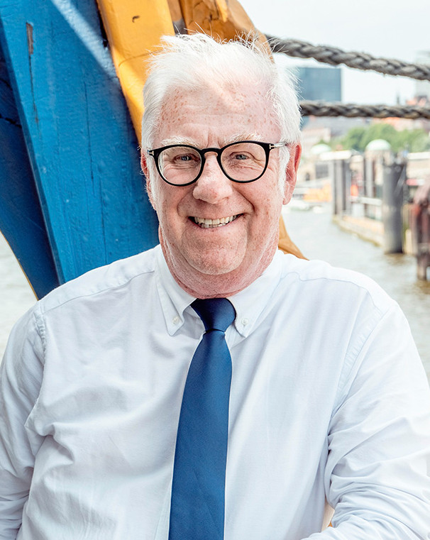 Medelålders man med glasögon ler mot kameran på en blå bakgrund