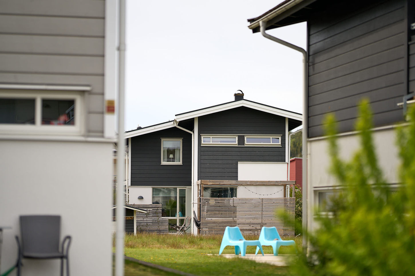 Modernt hus med svart fasad och gräsmatta; två blå stolar utomhus.
