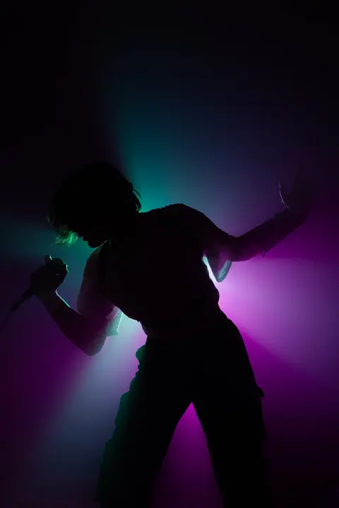 Silouette einer Sängerin vor einem Rosa-Grünen Hintergrund