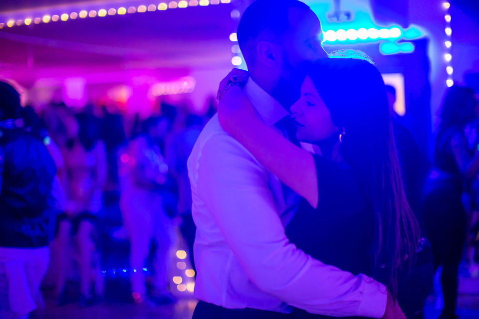A well-dressed and attractive couple dancing Kizomba in the foreground, with more Kizomba dancers in the background in soft focus