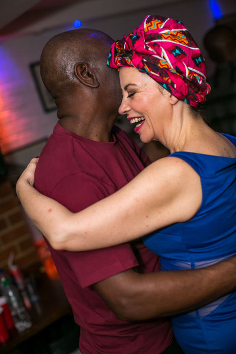 A man and a woman with a headwrap in a close embrace, gracefully dancing Kizomba together, with the woman smiling joyfully