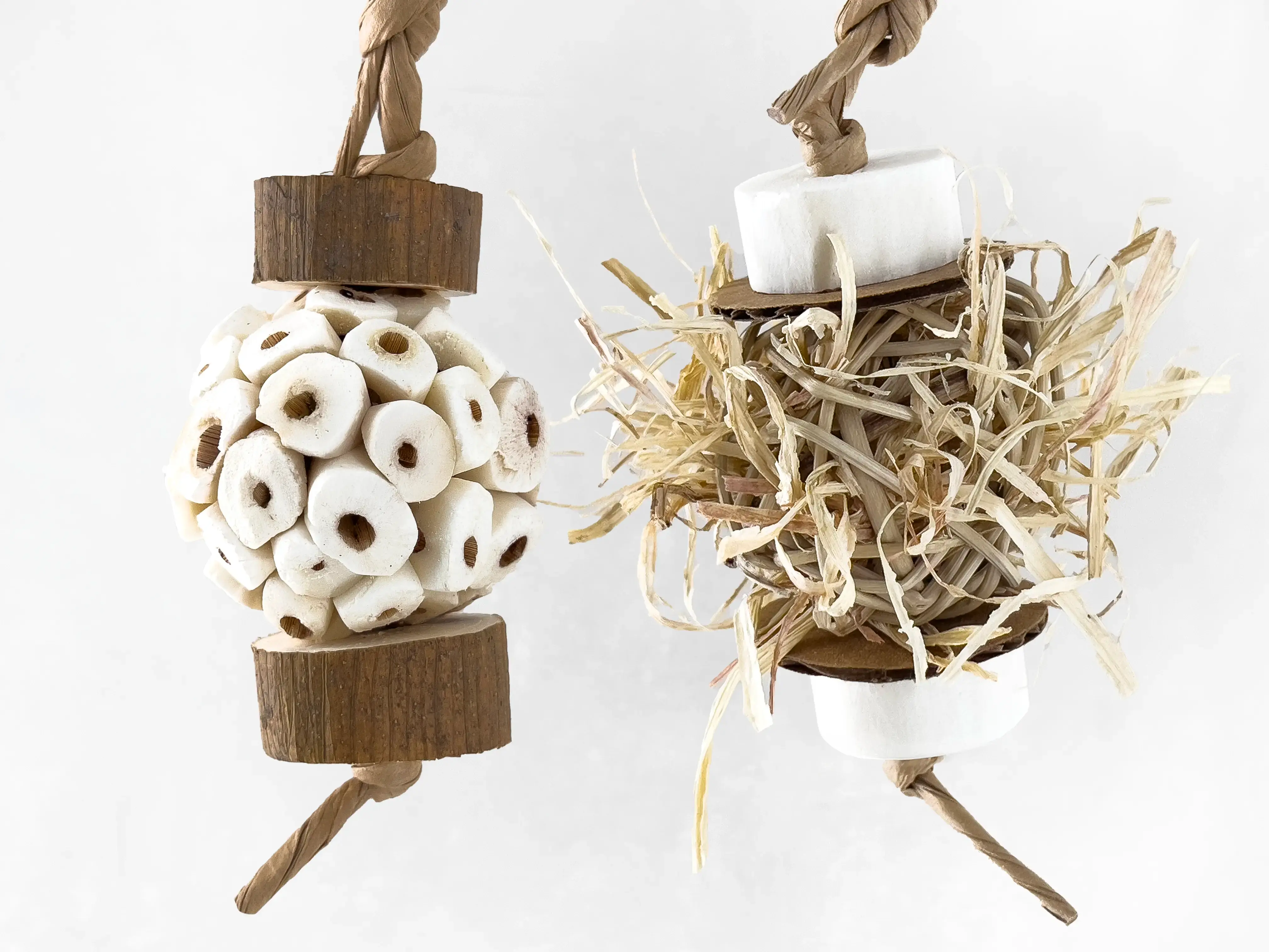 Two small bird toys handcrafted from sola wood, paper, vine ball, and corn husk for foraging and shredding.