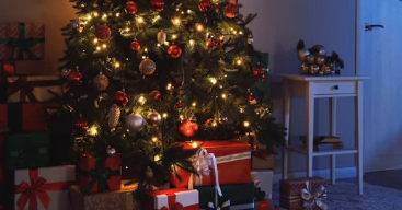 Christmas tree adorned with glowing lights and ornaments, surrounded by colorful presents. Cozy room with a small table and decorations.